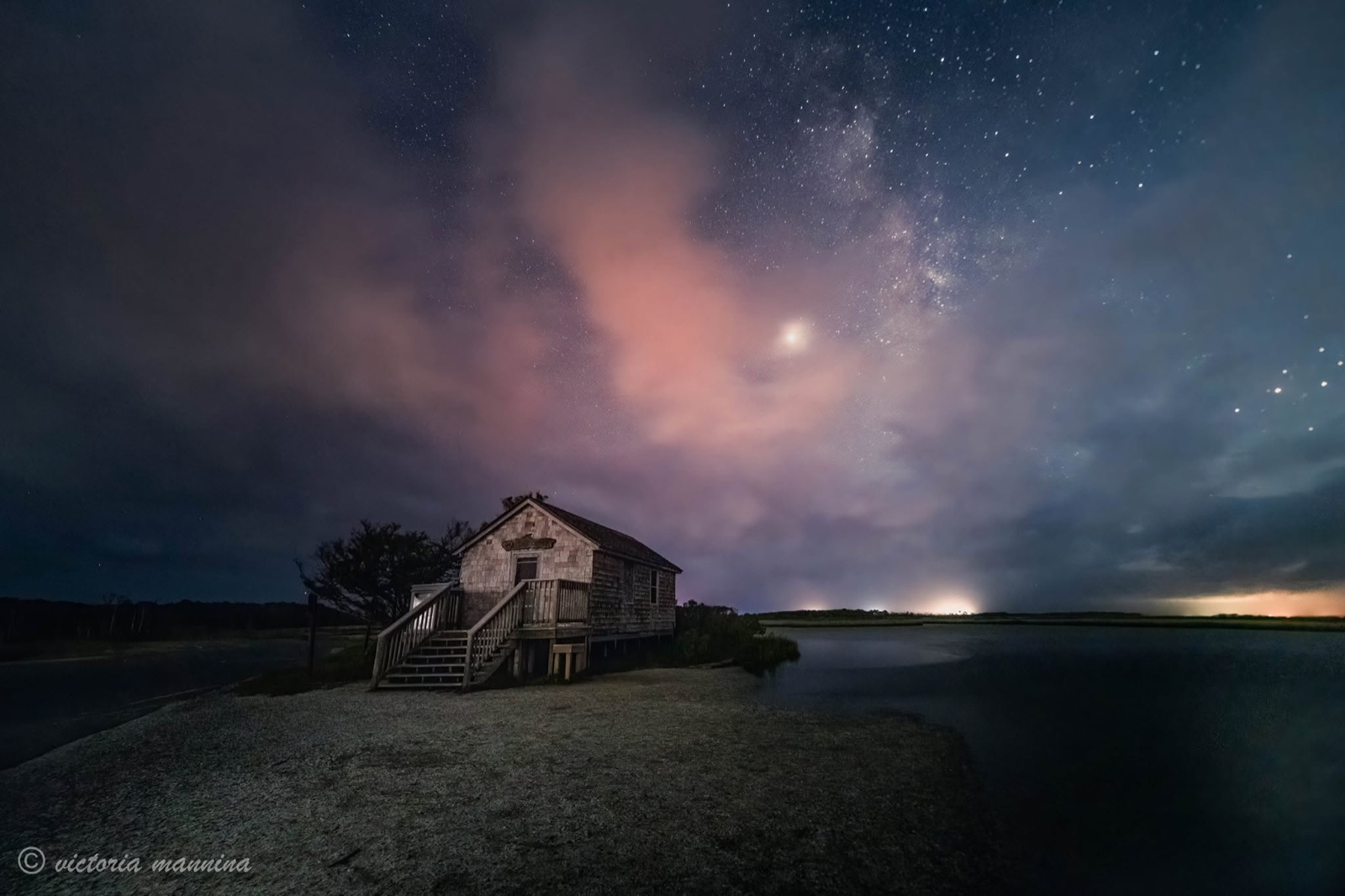 Weathered shoreline cabin beneath the Milky Way and glowing clouds