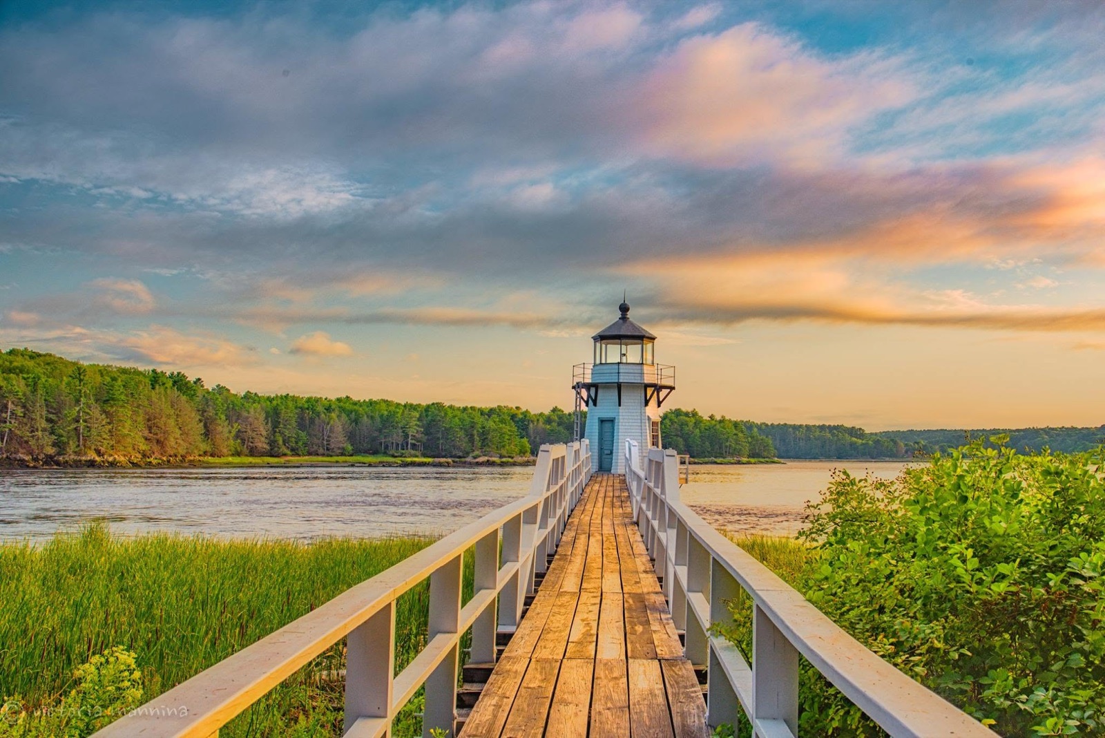 Wooden walkway leading to a lighthouse at sunset