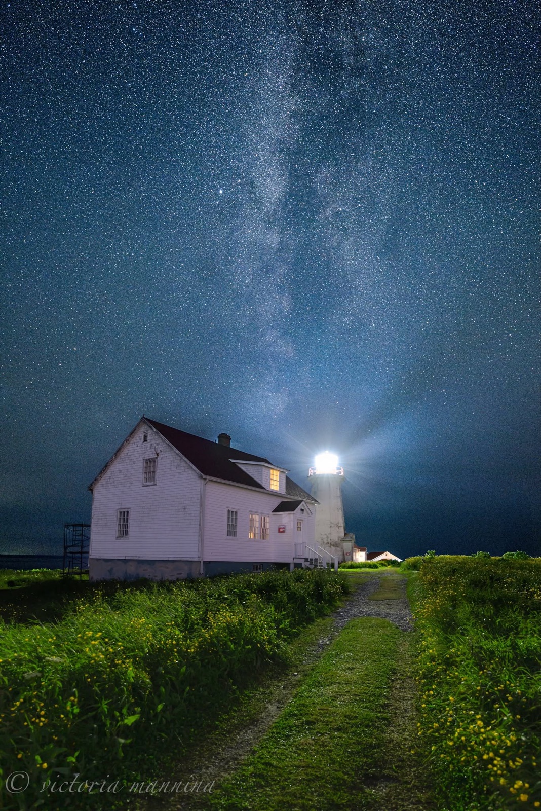 Keeper's house and lighthouse beam under starry night sky