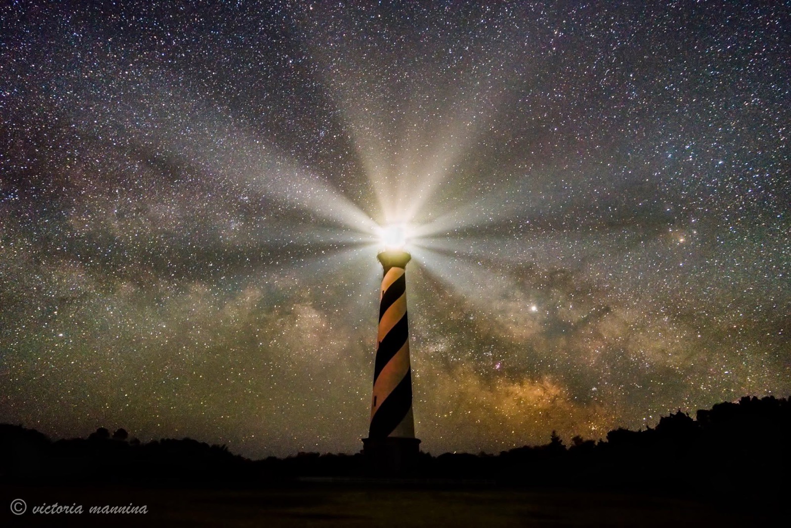 Lighthouse silhouette with beam under the Milky Way